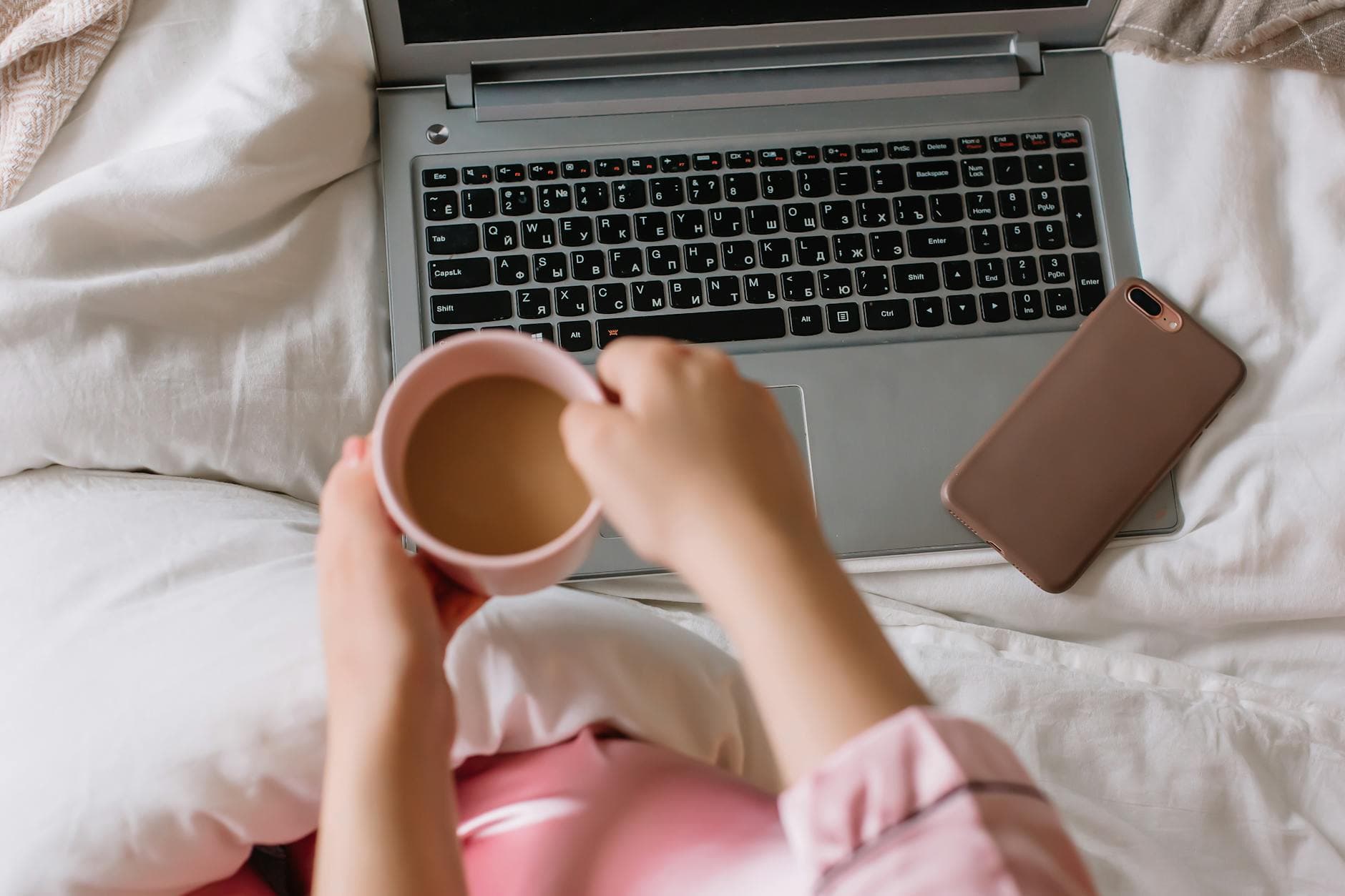 A relaxed morning scene showing hands holding a warm coffee cup next to a laptop on a wooden table.