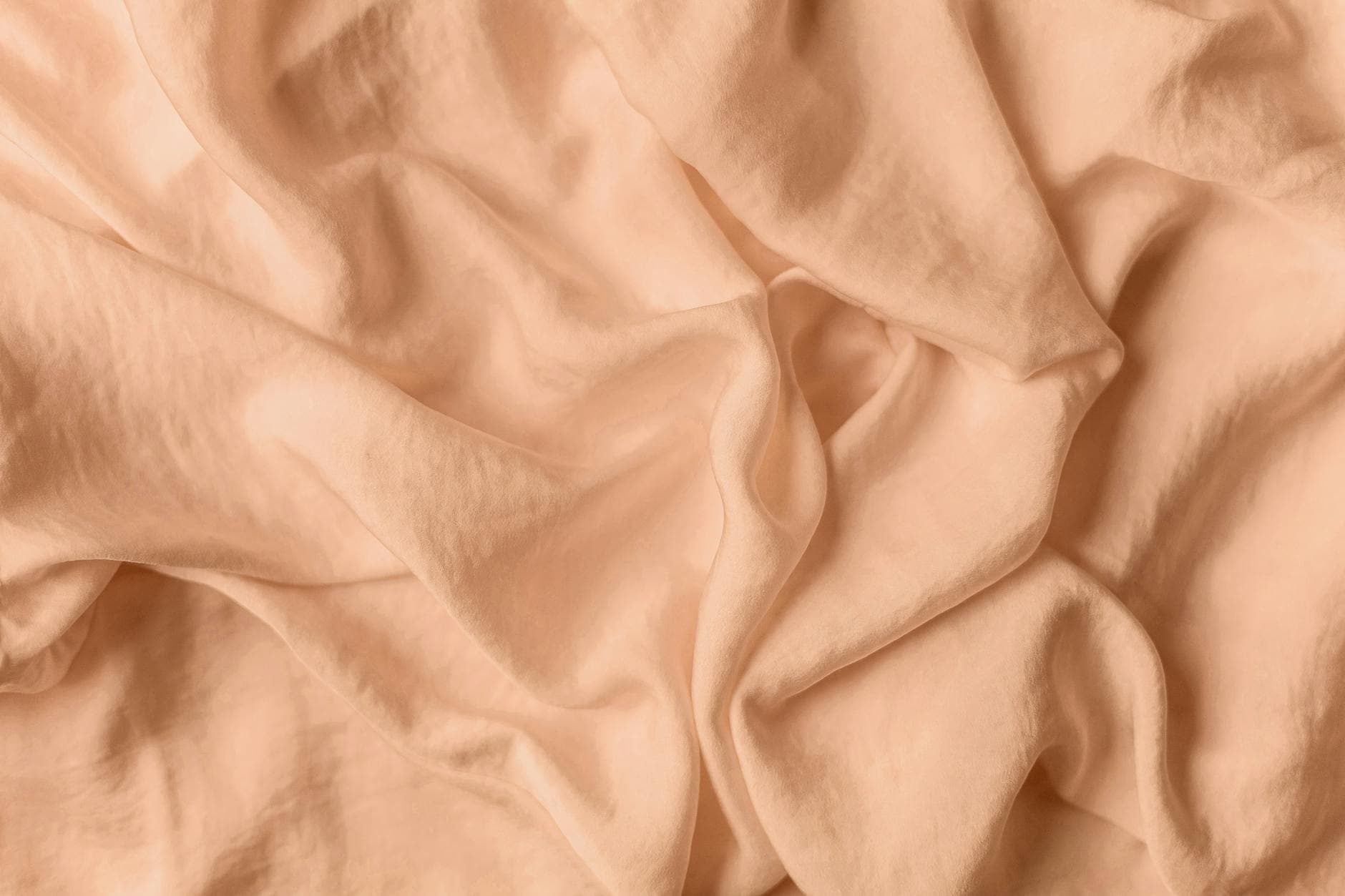 Soft, warm, light peach-colored linen fabric draping gracefully in morning sunlight.