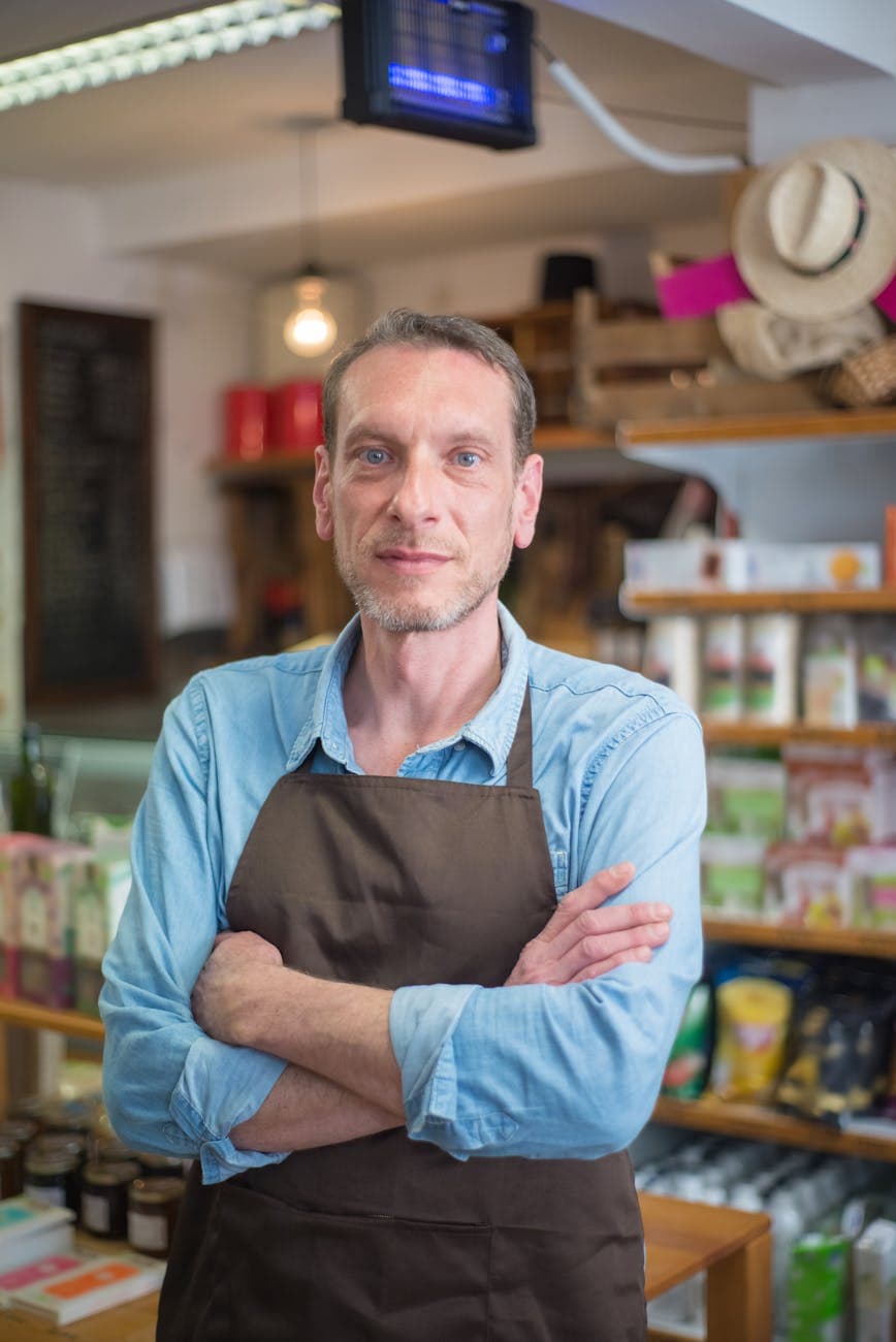 Portrait of Dana K., a small business owner standing with crossed arms in a warm apron.