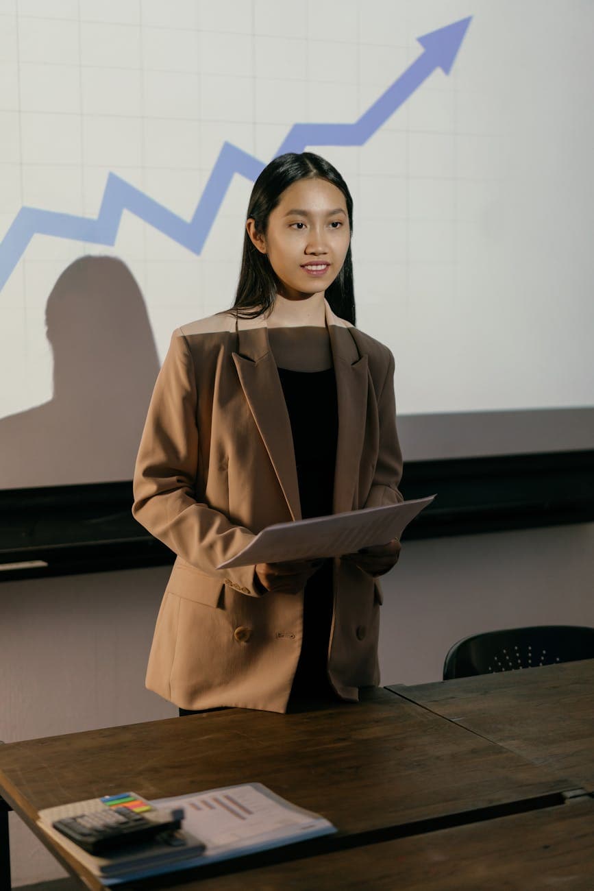 Portrait of Priya M., speaking confidently during a presentation in a modern room.